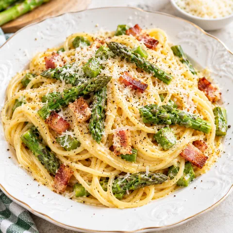 Carbonara ze szparagami, boczkiem i tartym serem na jasnym talerzu