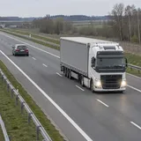 Samochód na lewym pasie przed ciężarówką, której przednie reflektory są rozświetlone.