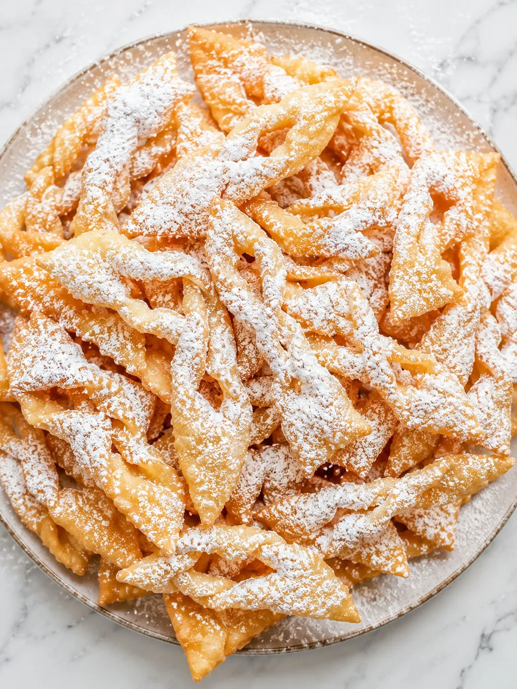 Top-down view of powdered sugar dusted faworki pastries stacked on a plate