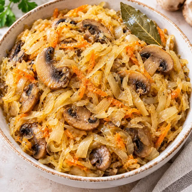 Kapusta z pieczarkami w jasnej misce z widoczną marchewką i cebulą