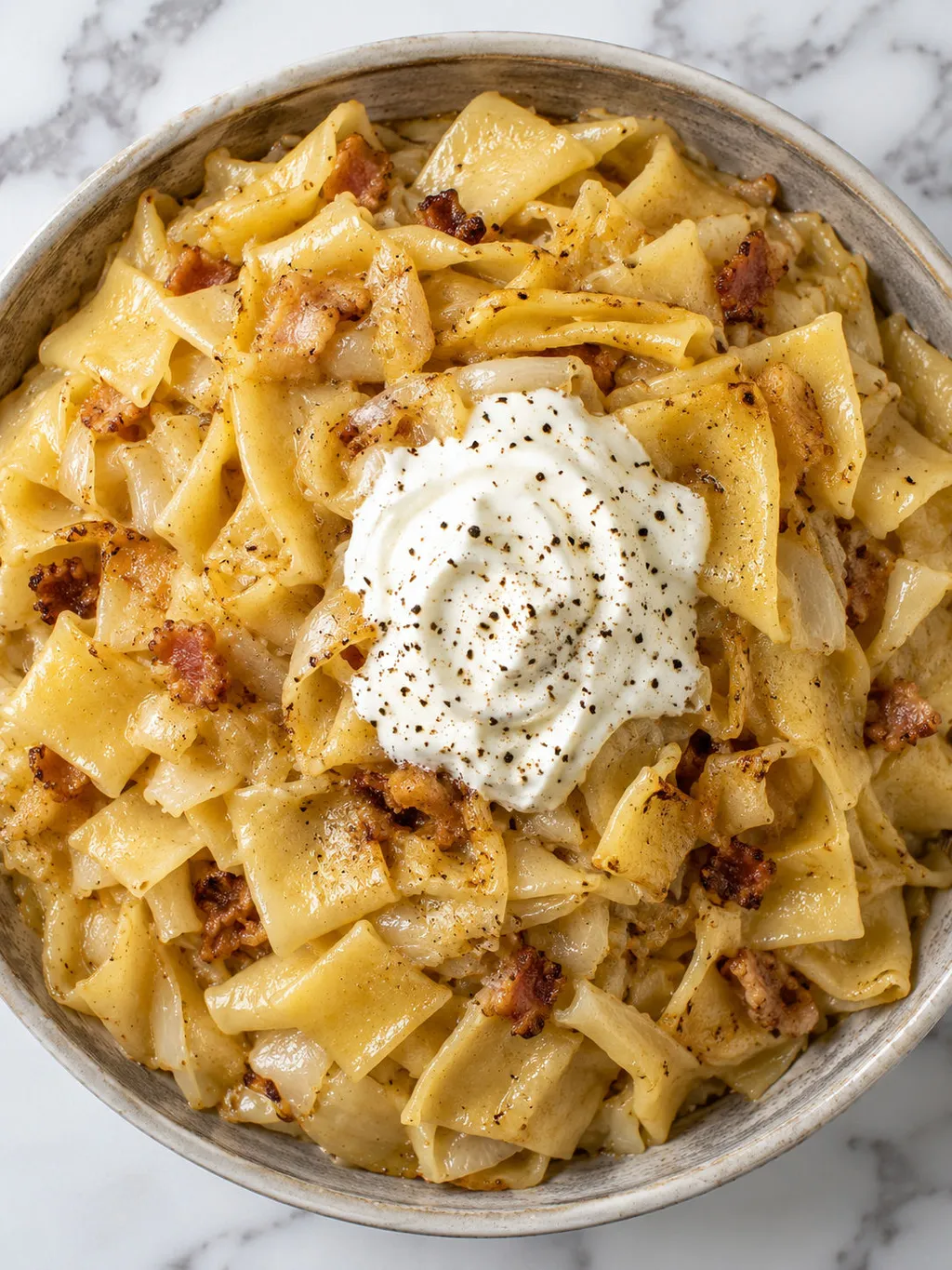 Top-down bowl of caramelized cabbage and egg noodles with sour cream