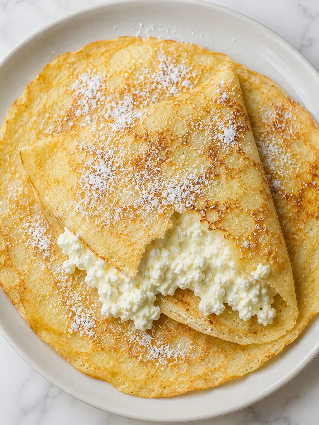 Top-down view of Polish cheese-filled crepes dusted with powdered sugar