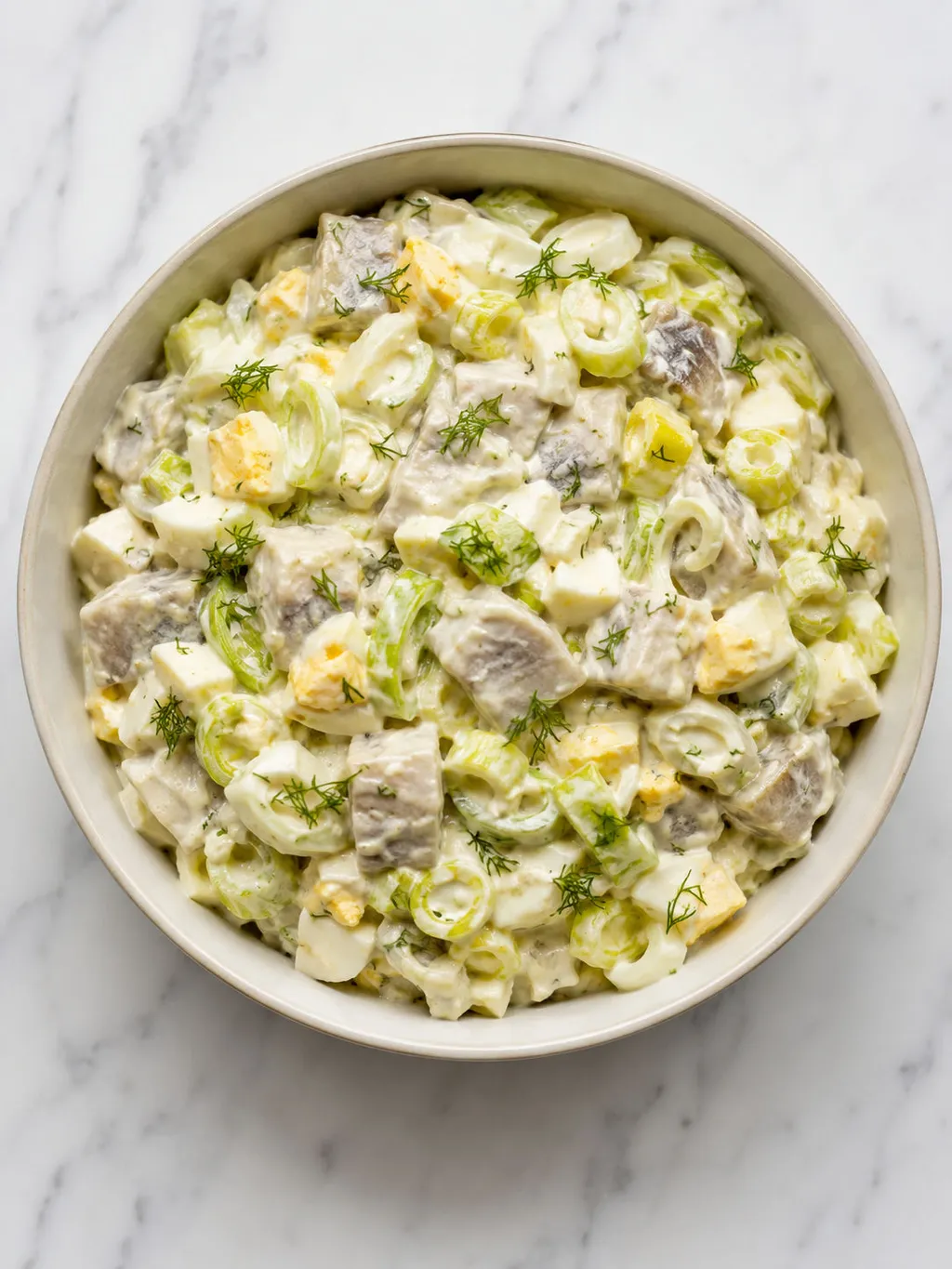 Top-down bowl of Polish herring salad with leek, egg and fresh dill