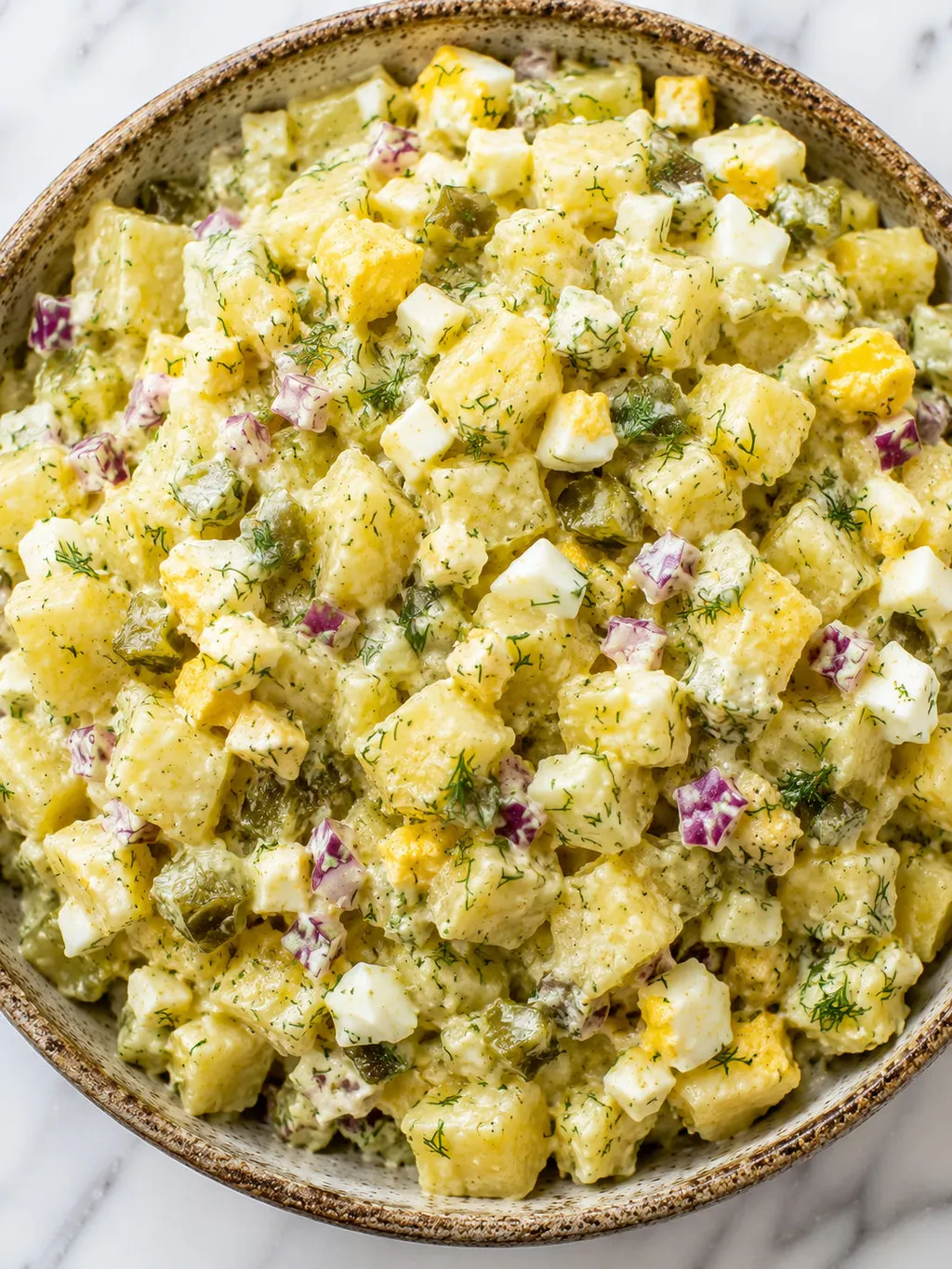 Top-down bowl of creamy Polish potato salad with dill pickles and fresh dill
