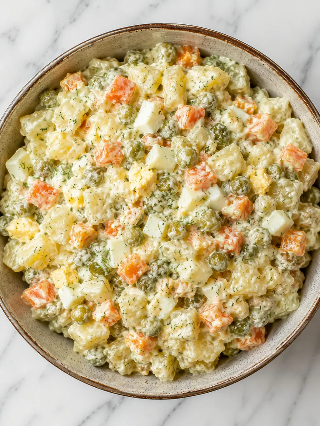 Top-down bowl of creamy Polish potato salad with pickles, carrots and dill