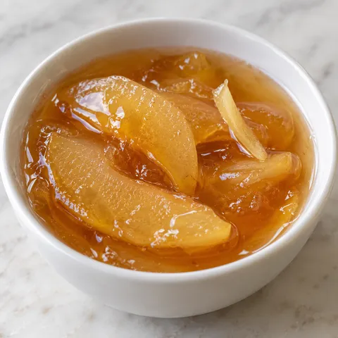Golden quince and ginger syrup in a glass bowl with ginger slivers