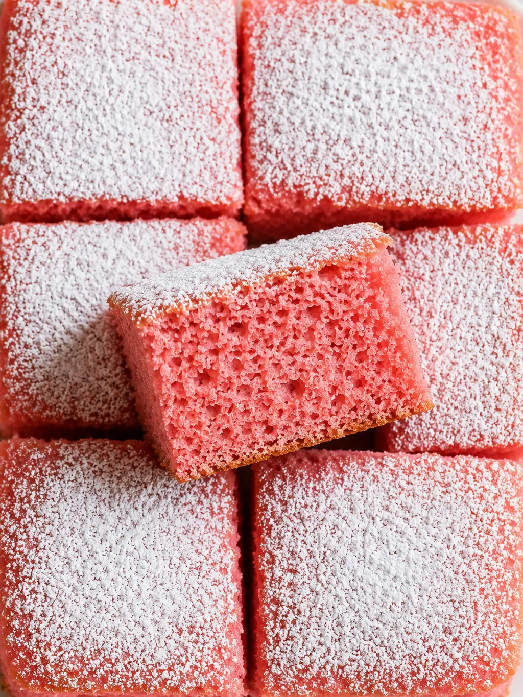 Puszyste różowe ciasto kisielowe pokrojone w kostkę i posypane cukrem pudrem